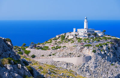 Lighthouse amidst sea and buildings against clear blue sky