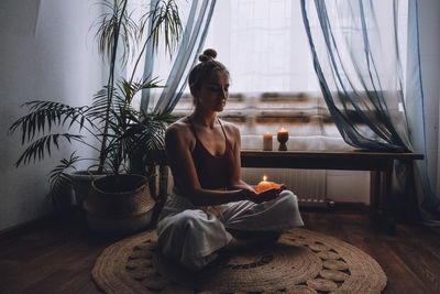 Young woman sitting on the floor, lights candles, enjoy meditation, do yoga exercise. mental health