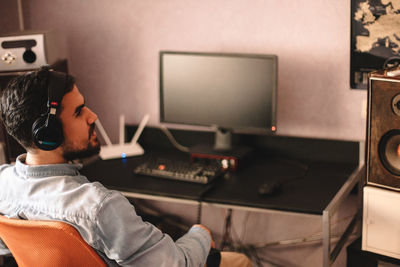 Young man listening music on headphones while sitting by computer