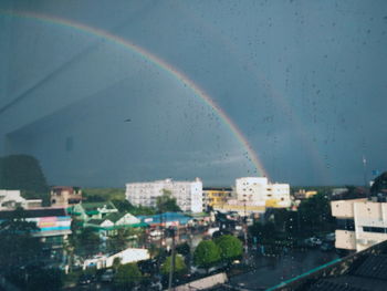 Rainbow over city buildings seen through wet window