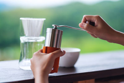 Closeup image of hand grinding coffee beans with manual stainless steel grinder to make drip coffee