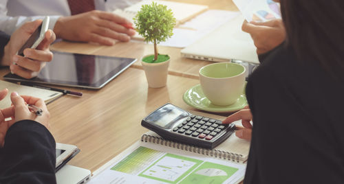 Midsection of woman using smart phone while sitting on table