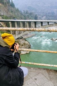 Side view of man photographing water on railing