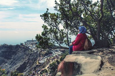 Rear view of woman sitting on rock against sky