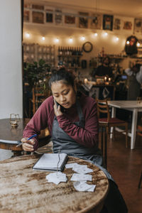 Female cafe owner talking on mobile phone while sitting with diary at table