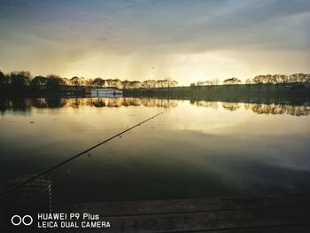 Fishing rod by lake against sky during sunset