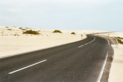 Empty road by snow covered land against sky