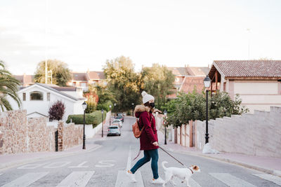 Full length of woman wearing mask walking on footpath in city against sky