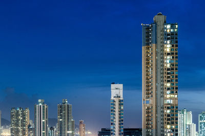 Illuminated skyscrapers against blue sky at night