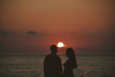 Silhouette people on sea against sky during sunset