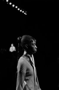 Side view of young woman looking away while standing against black background