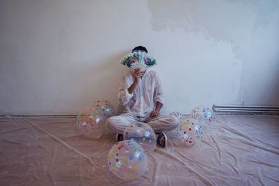 Woman covering face with hand fan while sitting amidst balloons