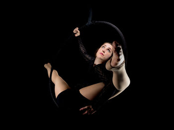 Low angle view of woman hanging on ring against black background