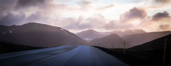 Panoramic shot of country road leading towards mountains against sky during sunset