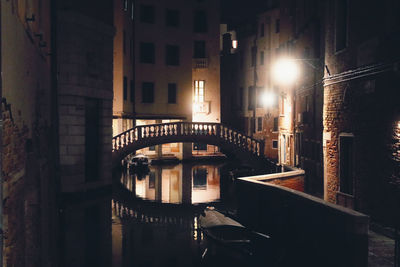 Illuminated bridge over canal by buildings at night