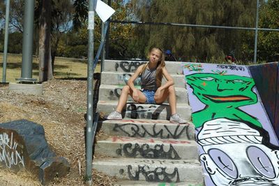 Full length portrait of girl sitting on graffiti steps at park