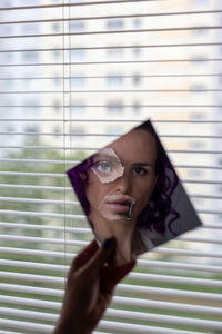 Portrait of woman holding mirror by window