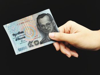 Close-up of hand holding paper over black background