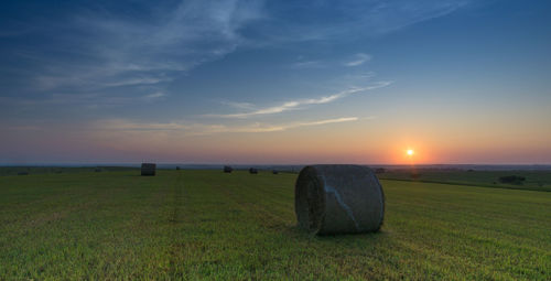 Hay bales on grassy field against sky during sunset