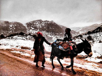 Men riding horses on snowcapped mountain against sky