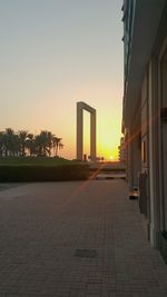 Footpath by palm trees and buildings against sky during sunset