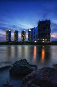 River by illuminated buildings against sky at dusk