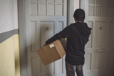 Rear view of delivery man with package standing at doorstep