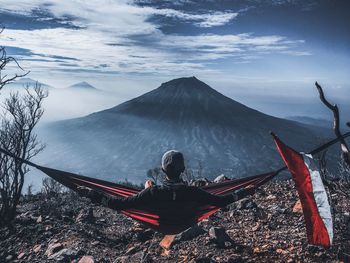 Rear view of man sitting on hammock against mountain