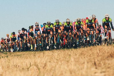 Cyclists riding bicycles on grassy field against clear sky