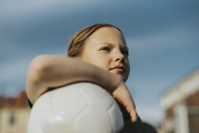 Contemplative girl with sports ball looking away against sky