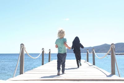 Rear view of kids running on jetty against sky