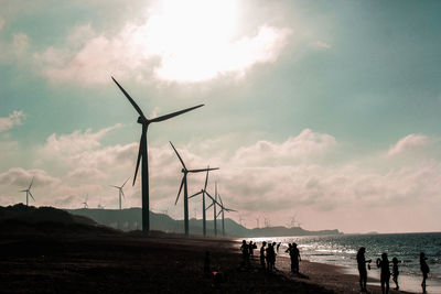 People with wind turbines on beach against sky