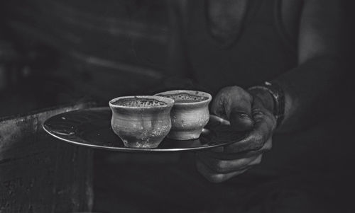 Midsection of man serving tea in mud cup on plate