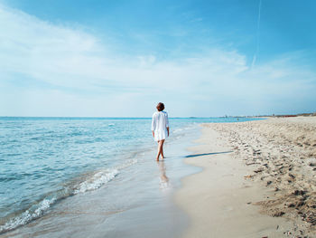 Young woman in cover up walking along the beach