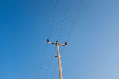 Low angle view of electricity pylon against clear blue sky