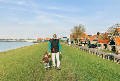 Mature man walking with granddaughter on grassy field by river in town