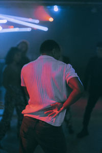Rear view of young man dancing under illuminated red light at nightclub
