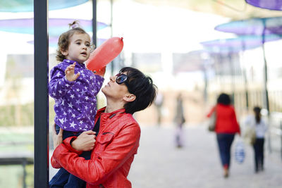 Mother carrying daughter on street in city