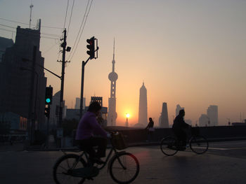 People riding bicycle on street against sky during sunset