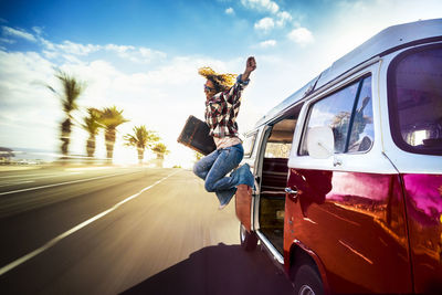 Cheerful woman jumping from van on street