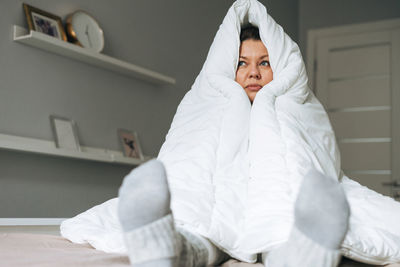 Young adult unhappy lonely woman forty years plus size body positive in white big blanket on bed 