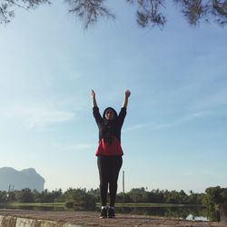 Full length of woman with arms raised exercising in park against sky