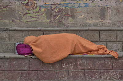 Person sleeping on footpath against wall