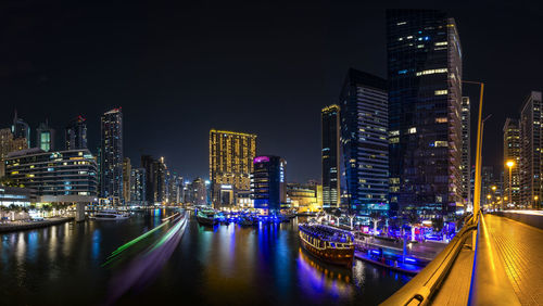 Illuminated buildings by river against sky at night