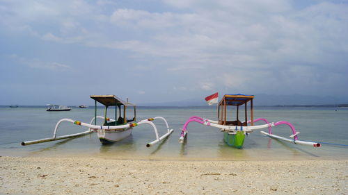 Outrigger canoe moored at beach against cloudy sky on sunny day