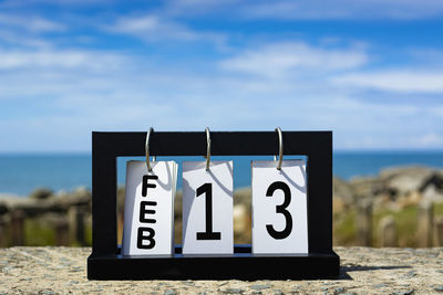 Close-up of information sign at beach against sky