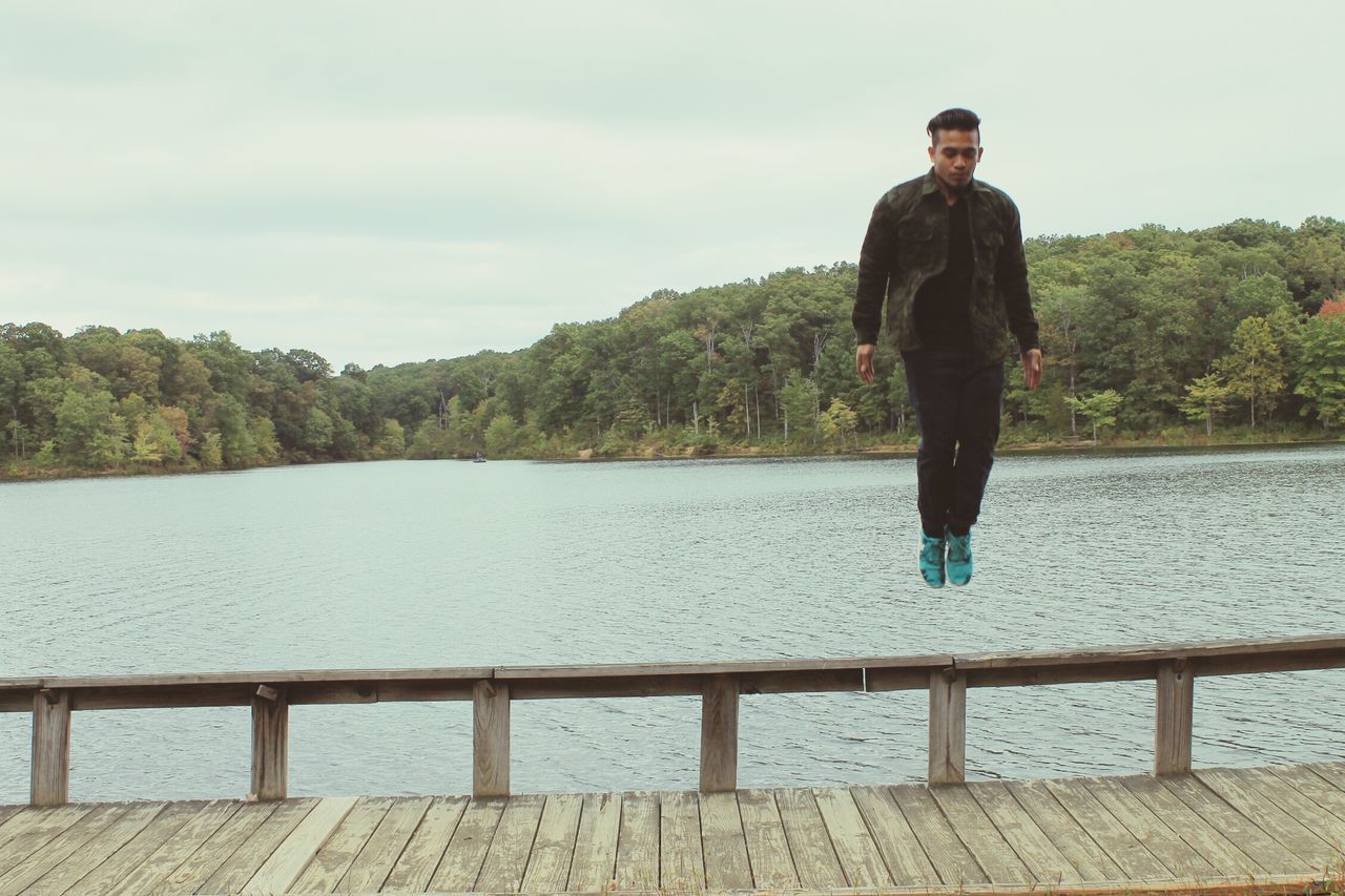 water, standing, lifestyles, leisure activity, sky, casual clothing, full length, lake, tree, tranquility, tranquil scene, young adult, railing, nature, scenics, beauty in nature, sea, river