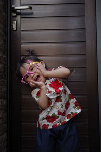 Cute girl wearing eyeglasses with mouth open standing against door