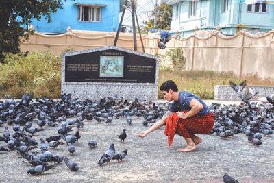 Full length side view of man feeding birds on street