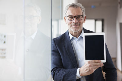 Successful businessman standing in his office holding digital tablet